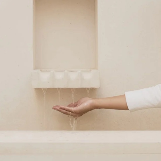 una mano debajo de un lavabo y pared de baño de cocina Piedra Paloma caliza